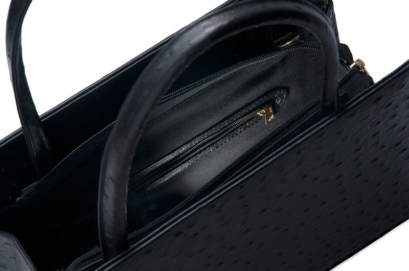 Inside zipper view black embossed ostrich leather bag with a raised front and back panel and attached handles. Top zip closure with an inside zipper pocket and two open pockets. Interior consists of high quality black cotton lining. Comes with a detachable shoulder strap with an adjustable buckle.