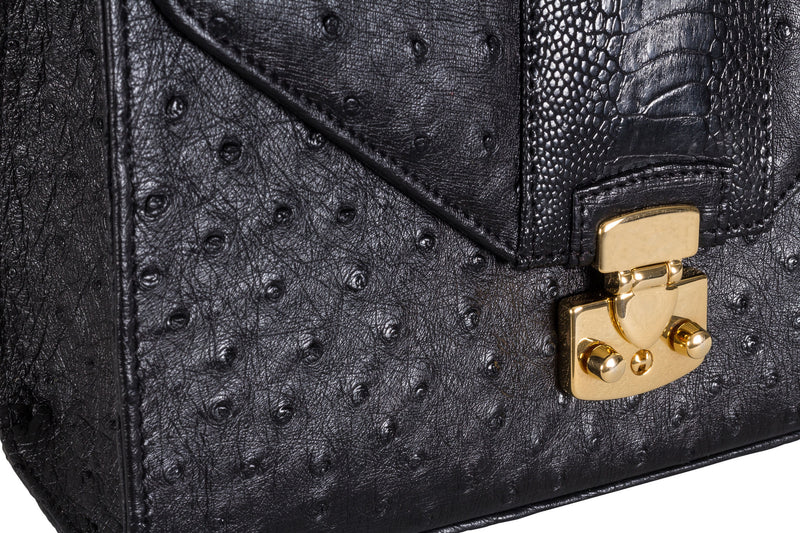 Detailed view black ostrich and shin constructed top flap handbag with an Italian lock closure. Contains inside back zipper pocket and a front inside zip pocket. High quality black leather interior. Includes a top handle with 24 carat gold plated fittings, detachable shoulder strap, adjustable buckle. Bottom bag feet studs.