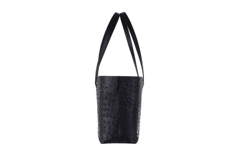 Side view black ostrich leather shopper style bag with two shoulder straps and decorative hardware. Magnetic top closure. Suede leather lining and multiple Inside pockets. 