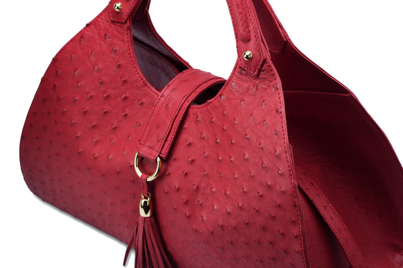 Top front side view Kimberley red ostrich Leather bag with fold over magnetic strap with D-ring & tassel decoration. Attached round shaped handles decorated with a studs. 