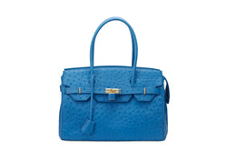 Front view ostrich leather bag with top zip. The interior contains an inside zip pocket with two internal patch pockets, and is lined with high quality black suede leather. Features a double handle and a gold lock system as decorative hardware. Bag feet studs are located on the bottom panel of the bag.