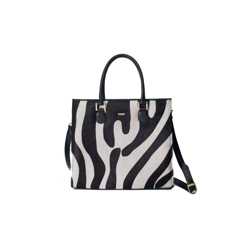 Linda front view with strap. Black bovine leather side, back and bottom panel, with white and black zebra printed hair on hide on the front panel. Contains an inside zipper with a back-zip pocket. The bag interior consists of high-quality black cotton suede lining. Includes a top zip closure with gold plated hardware, and a detachable shoulder strap with an adjustable buckle. Bag feet studs are located on the bottom panel.